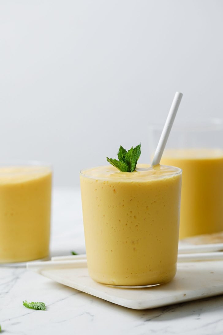 Mango Lassi in clear glasses topped with mint with a straw inside