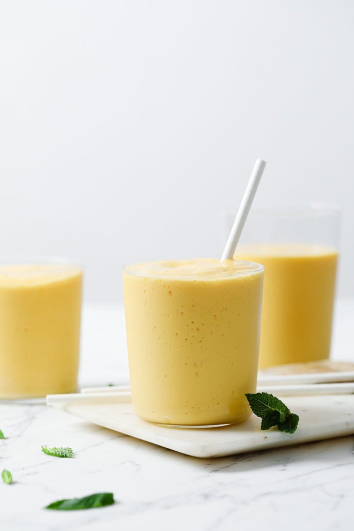 Mango Lassi in clear glasses topped with a straw inside