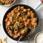 Aloo Baingan in a skillet with naan and yogurt on the side