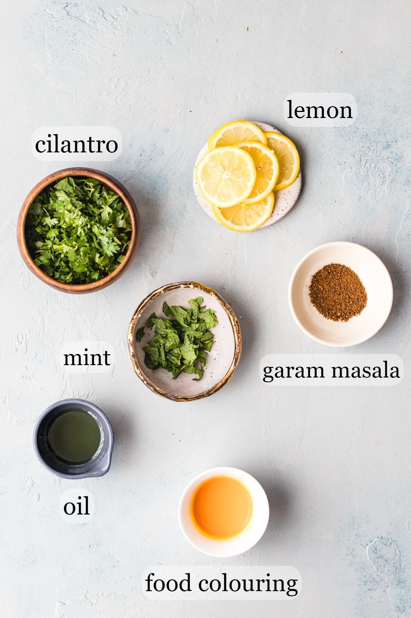 Ingredients for layering and topping the chicken biryani such as cilantro, mint, lemon slices, oil, and food colored milk