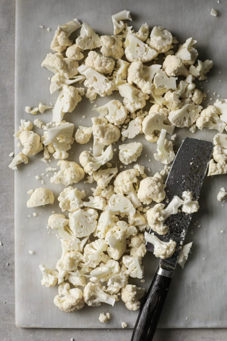Chopped cauliflower on a cutting board with a knife on the side