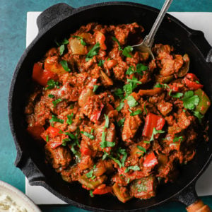 Chicken Jalfrezi in a black skillet with a silver spoon