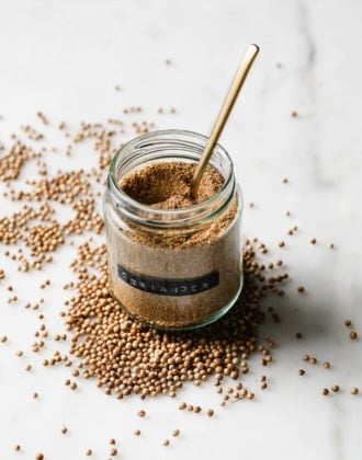 Coriander powder in a small spice jar with a gold spoon.