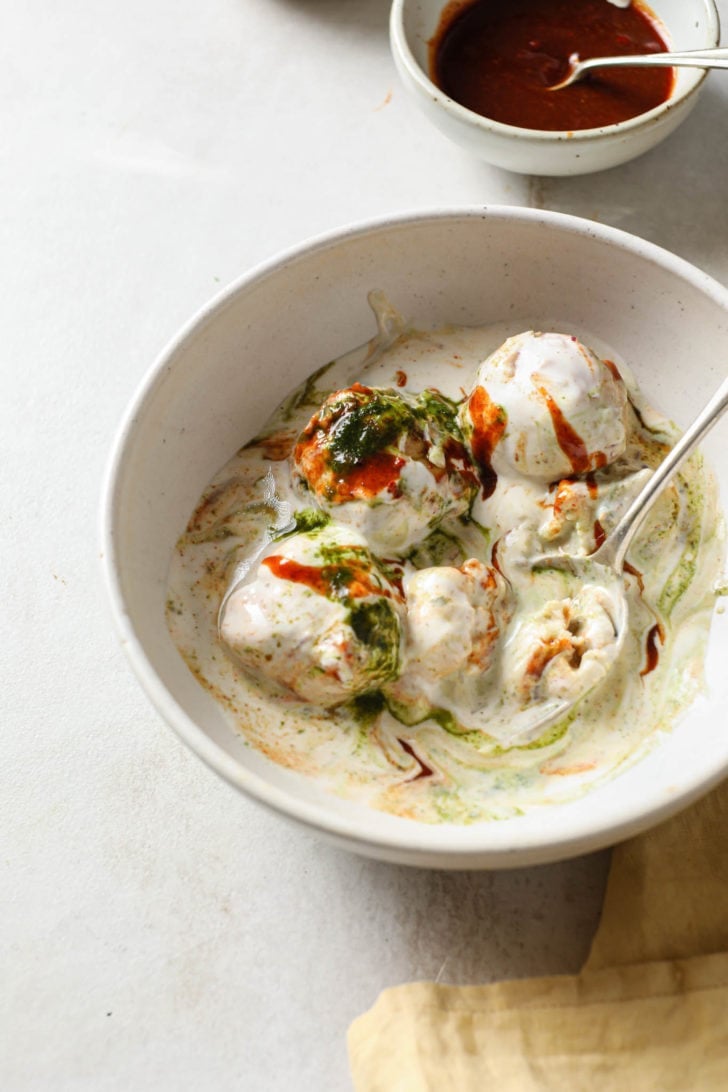 Partly eaten Dahi bhallas in a white bowl with a silver spoon. 