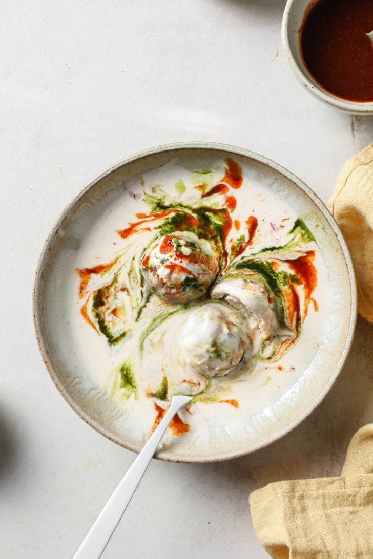 Dahi Bhallas partly eaten in a bowl with silver spoon.