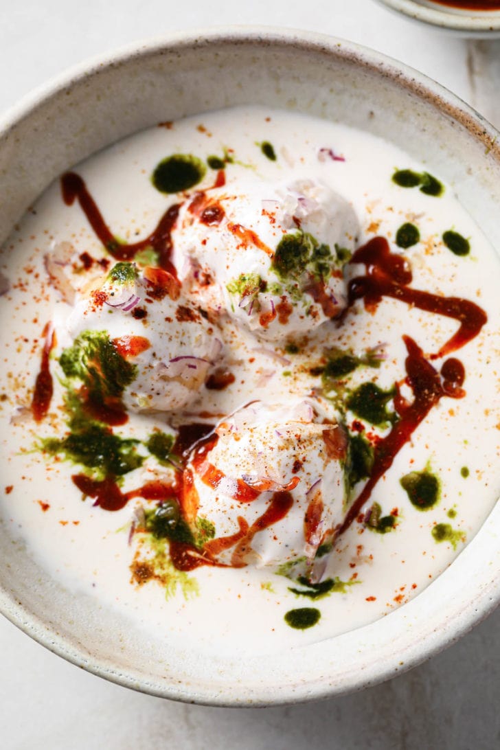 Closeup of Dahi Bhalla in bowl garnished with chutneys and spices.