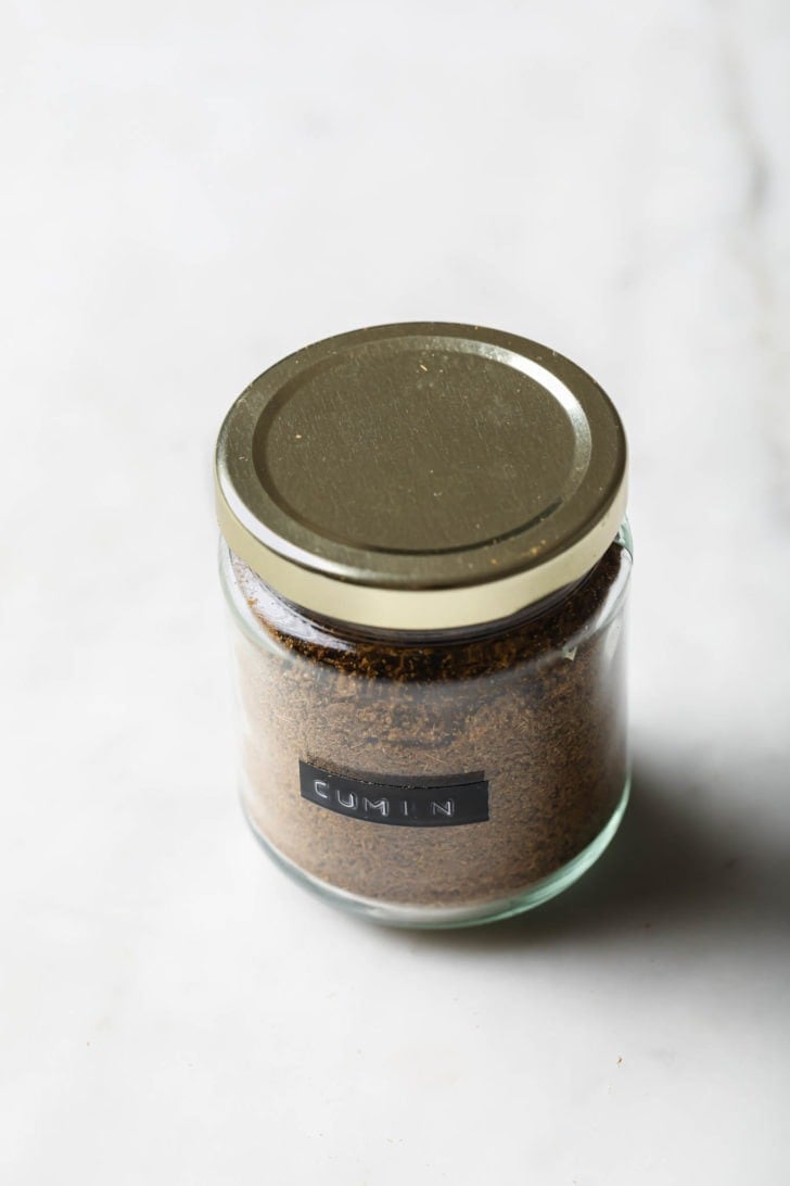 Cumin powder in a labeled, covered glass jar.
