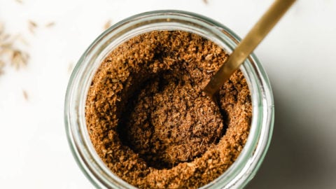 Top view of a jar of cumin powder with a golden spoon inside.