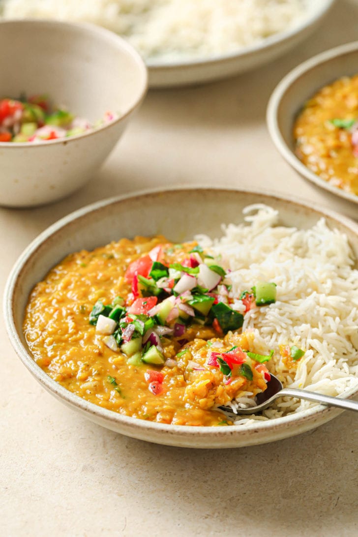 A bowl with rice and Masoor Dal topped with crunchy vegetables.