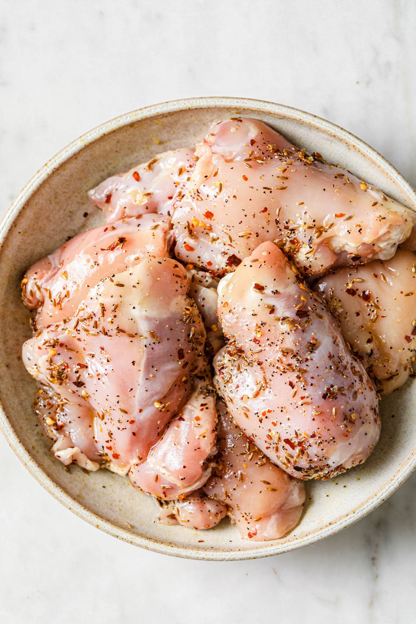 Uncooked bone-in skinless chicken thighs in a bowl.