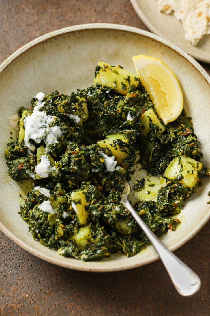 Aloo palak in a bowl with some yogurt and a fork.