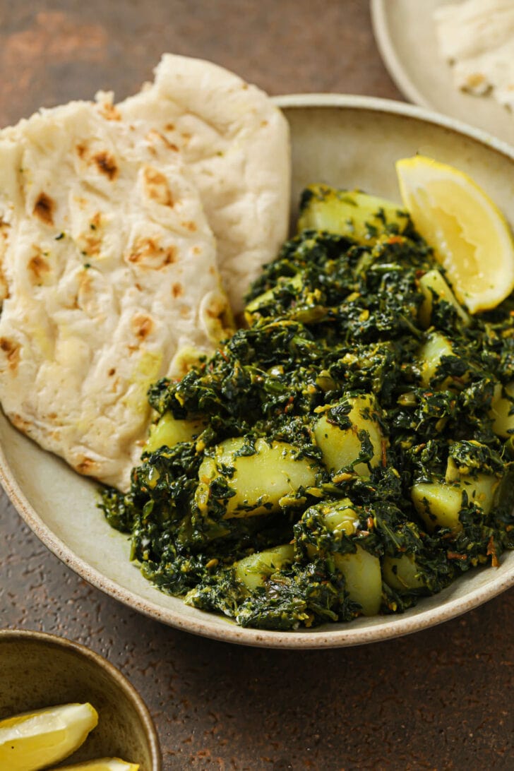 A plate of Aloo Palak with naan and a lemon wedge.