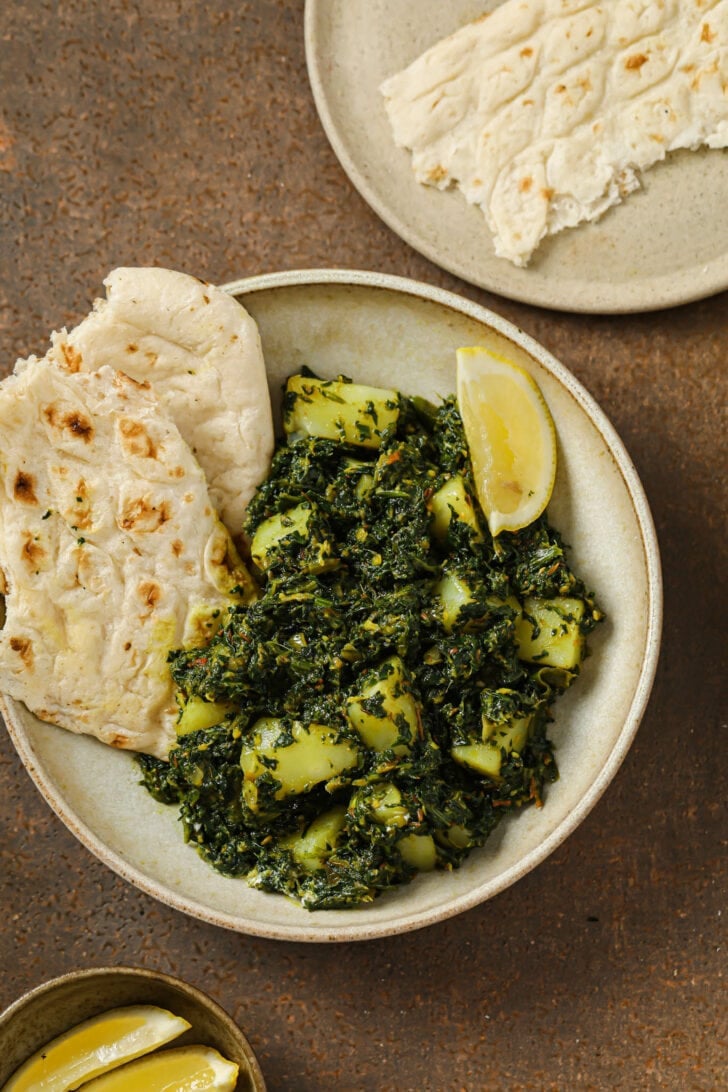 A plate of Aloo Palak with naan and a lemon wedge.