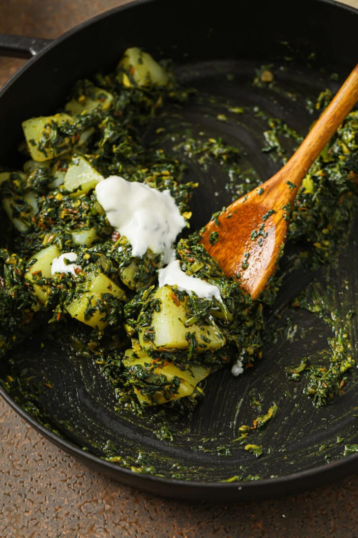 Close up of Aloo Palak in skillet topped with dollops of yogurt.