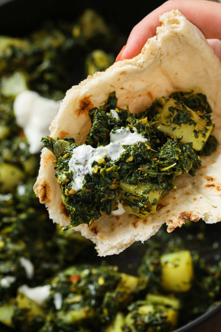 Holding some Aloo palak with yogurt in a piece of naan.