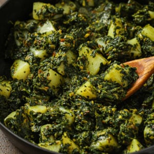 Close up of Aloo Palak in a skillet with a wooden spoon.
