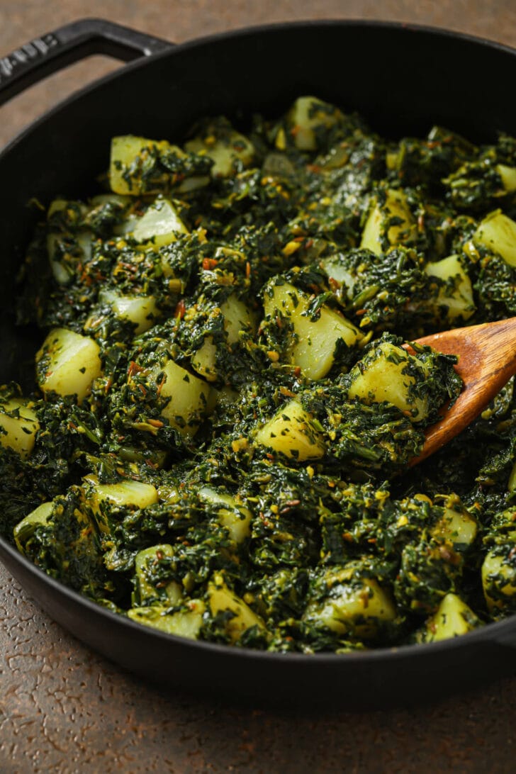 Close up of Aloo Palak in a skillet with a wooden spoon.