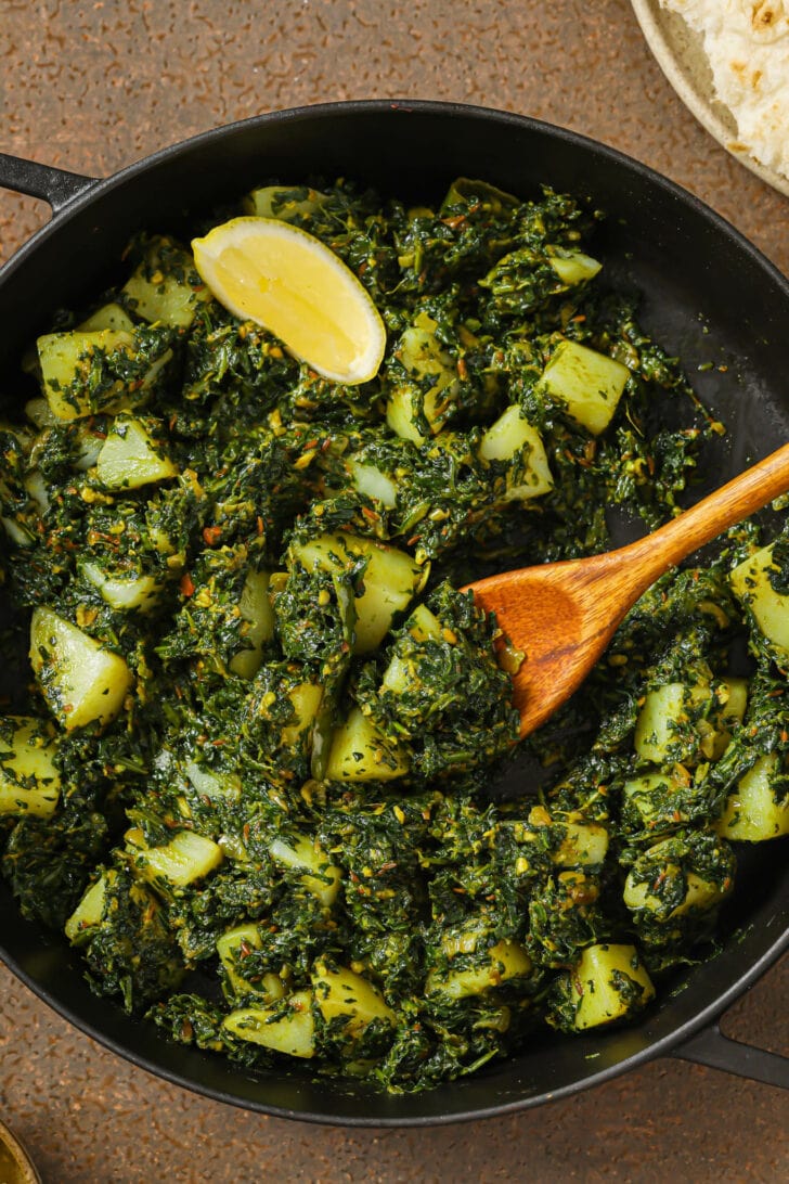 Aloo palak in a skillet with a wooden spoon.