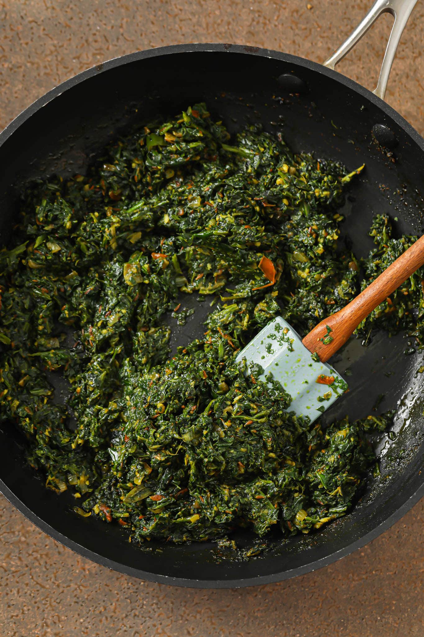 Cooked down spinach-onion-tomato mixture in a skillet with a blue spatula.