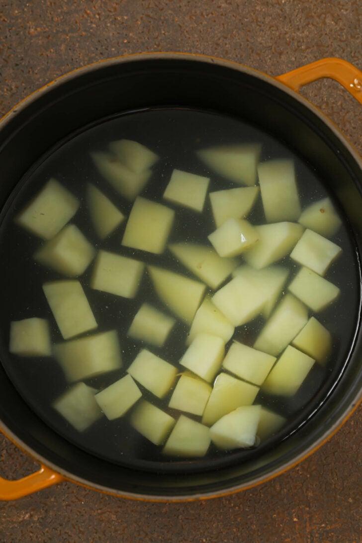 Peeled cubed potatoes pieces in a pot filled with water.