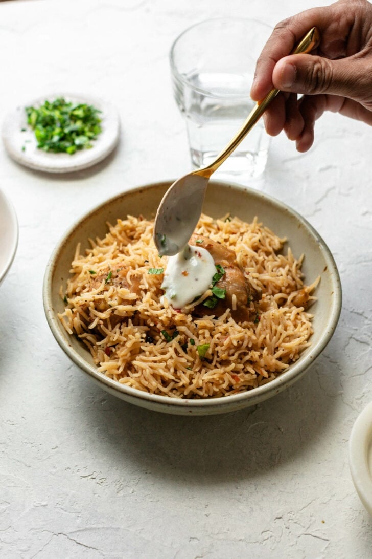Adding a dollop of yogurt to a bowl of Chicken Pulao.