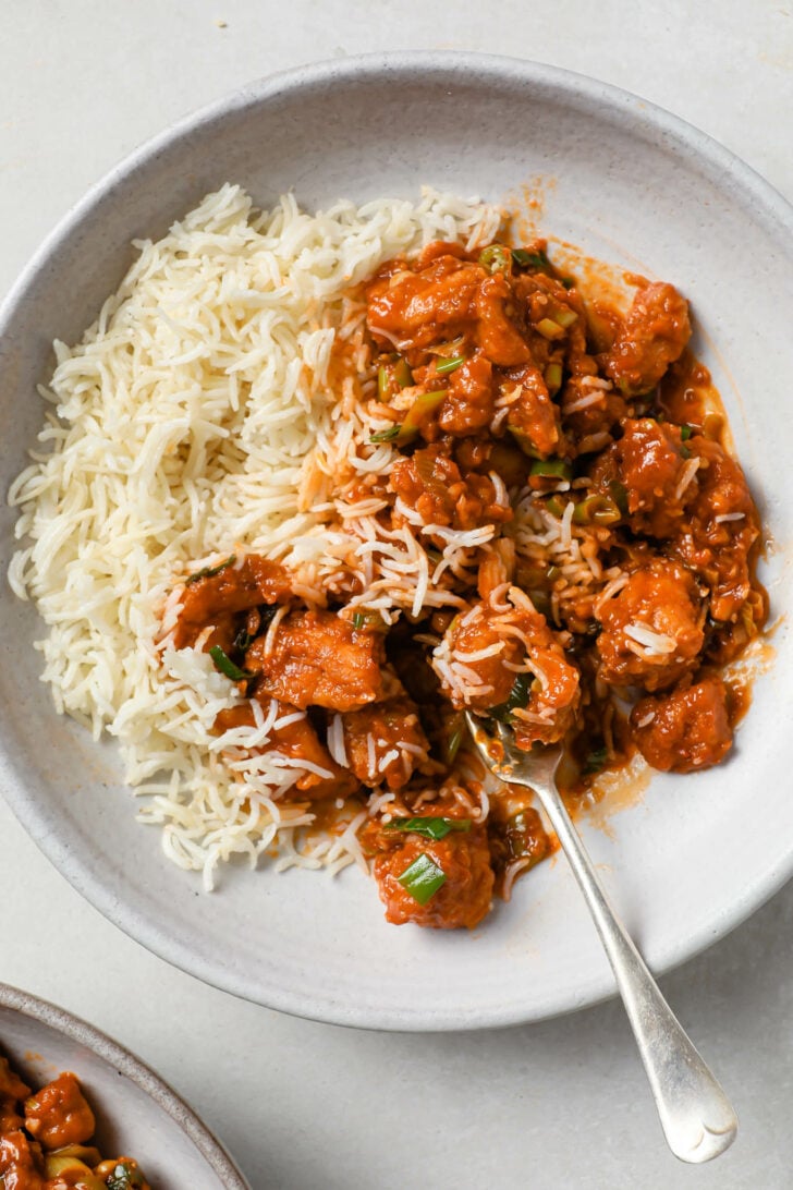 Partially eaten Chicken Manchurian with rice and a fork.
