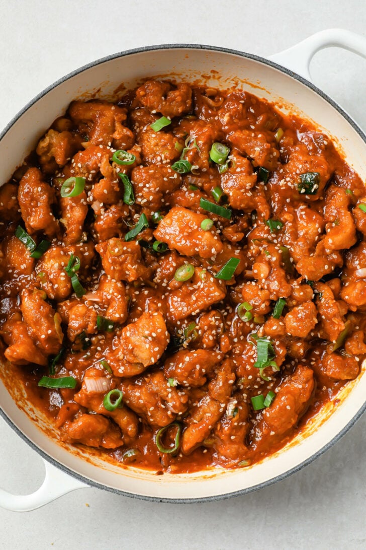 Manchurian chicken in a pot garnished with sesame seeds and green onion.