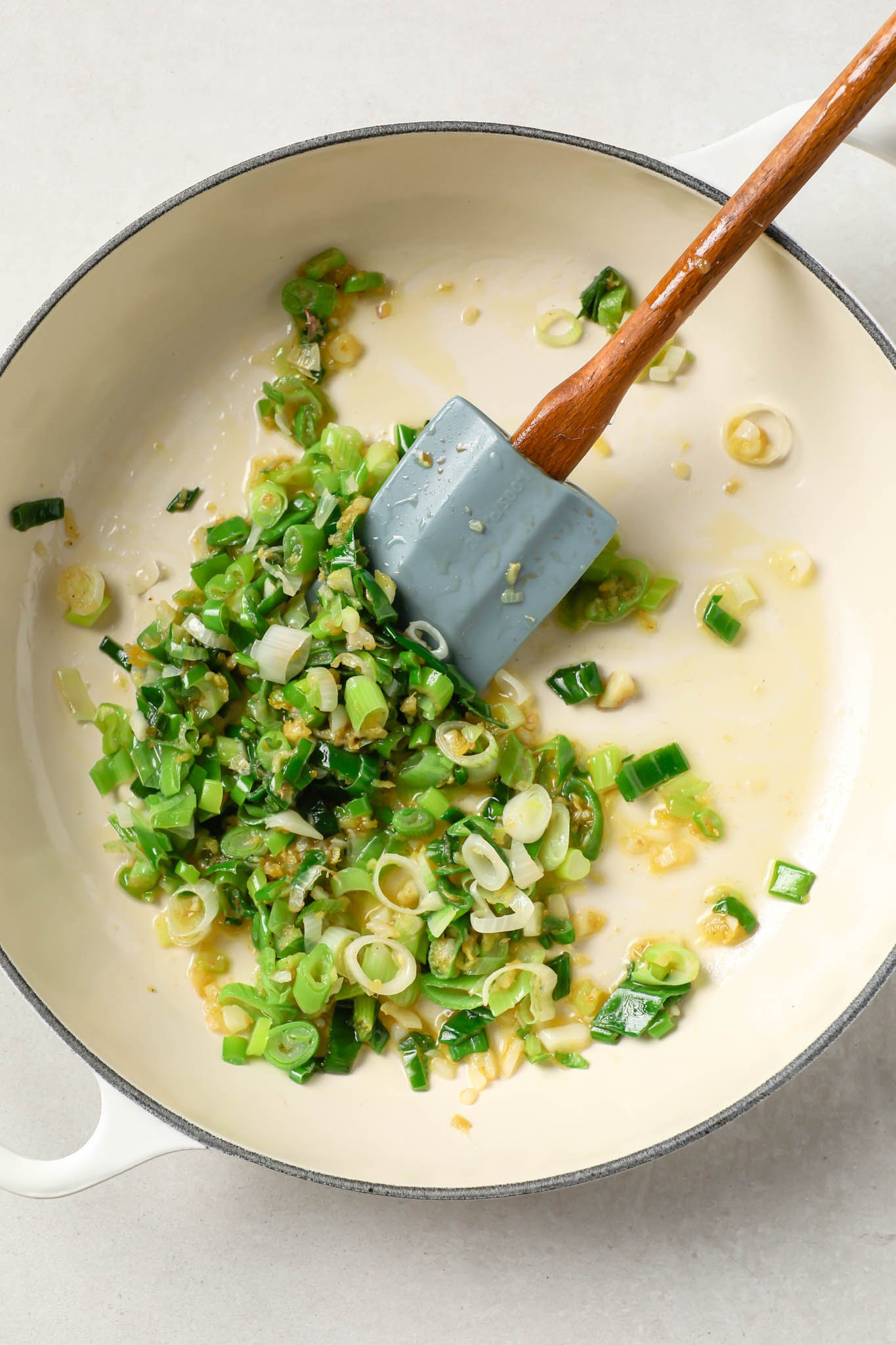 Sautéed green onions in a pot with a rubber spatula.