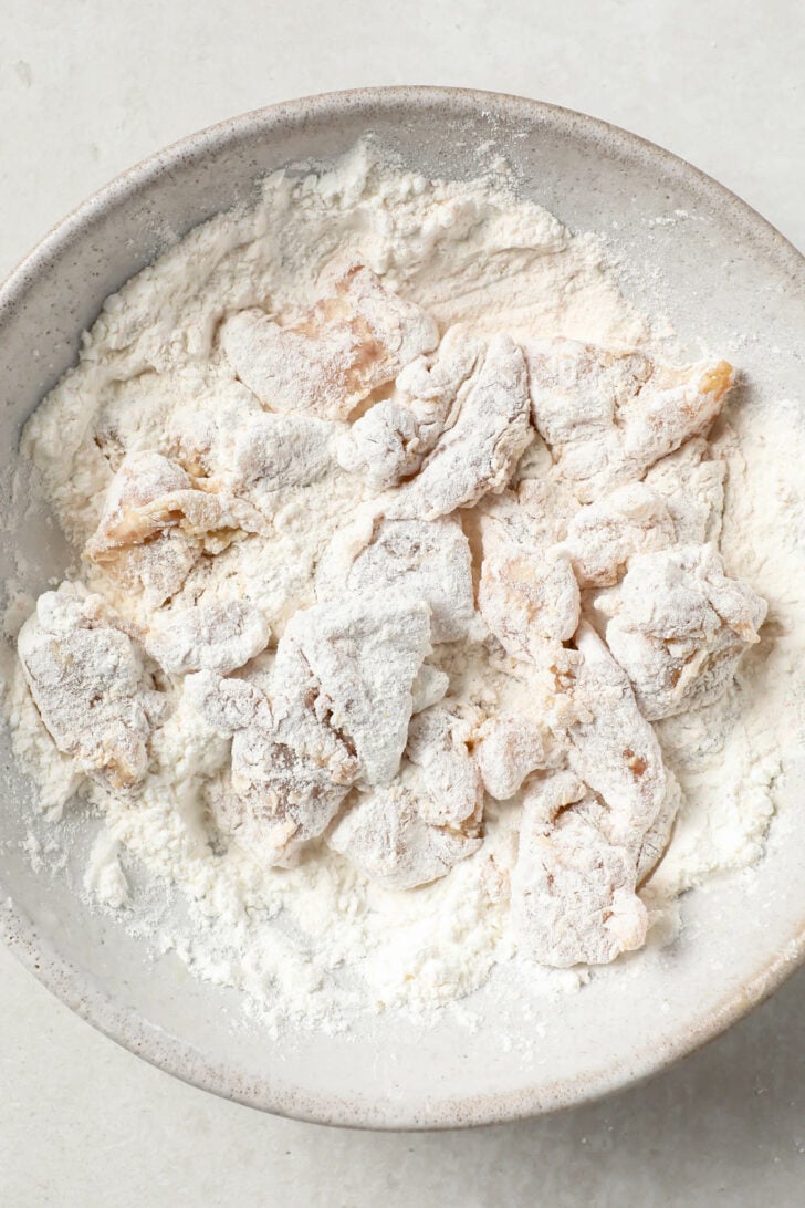 Marinated chicken coated in dry coating in a white bowl.