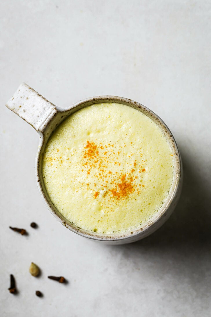 Top view of a speckled mug filled with Turmeric Milk with some turmeric powder dusted on top.