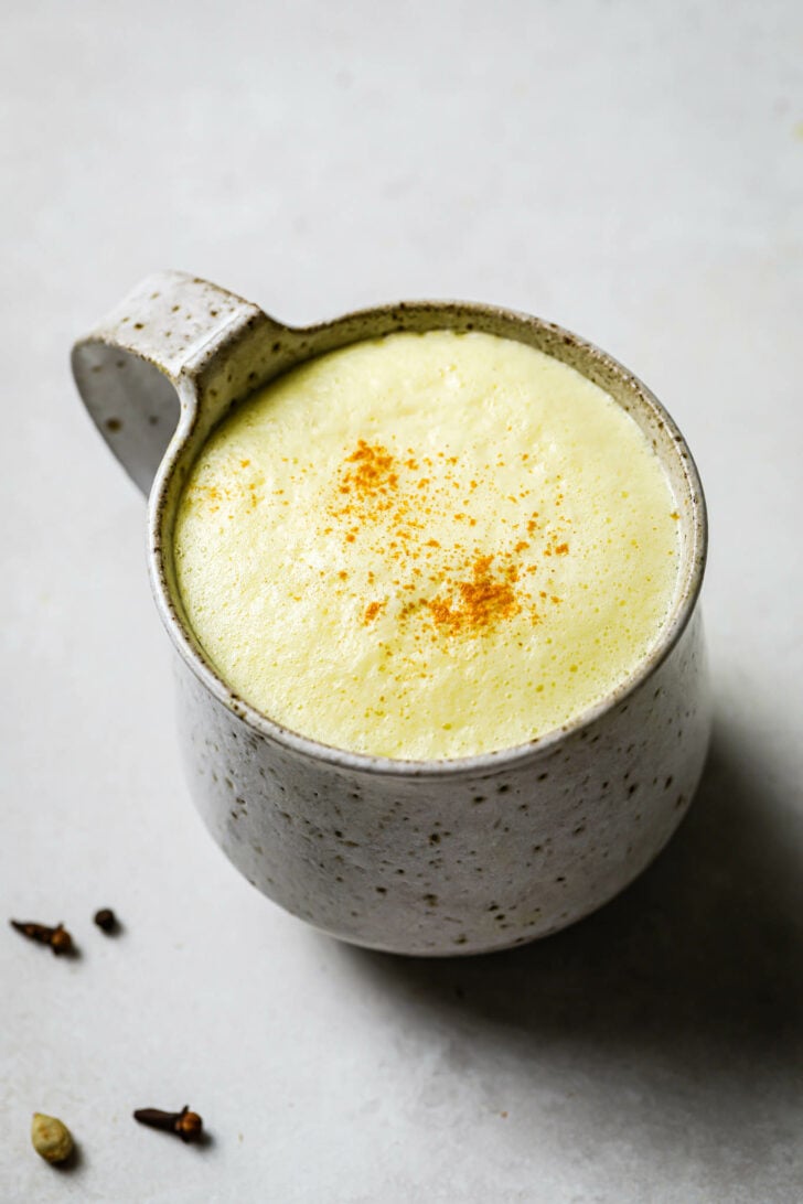 A speckled mug filled with Turmeric Milk with some turmeric powder dusted on top.