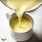 Pouring Turmeric Milk from a pot into a speckled mug.
