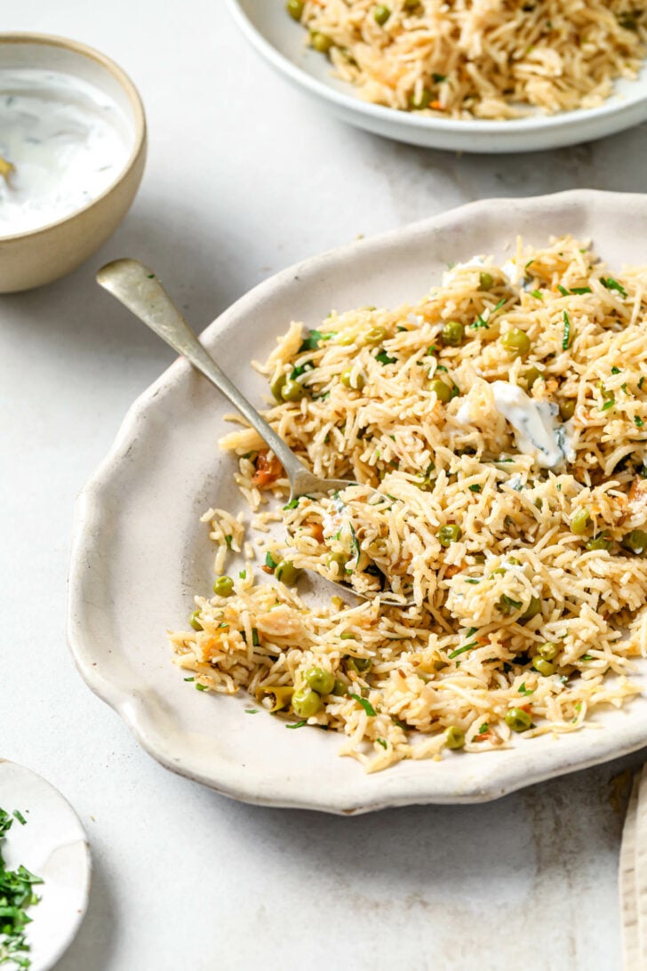 Matar Pulao on a platter garnished with cilantro and dollops of raita.