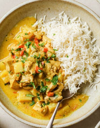 Chicken Curry with Coconut Milk and rice in a beige bowl with a metal spoon.