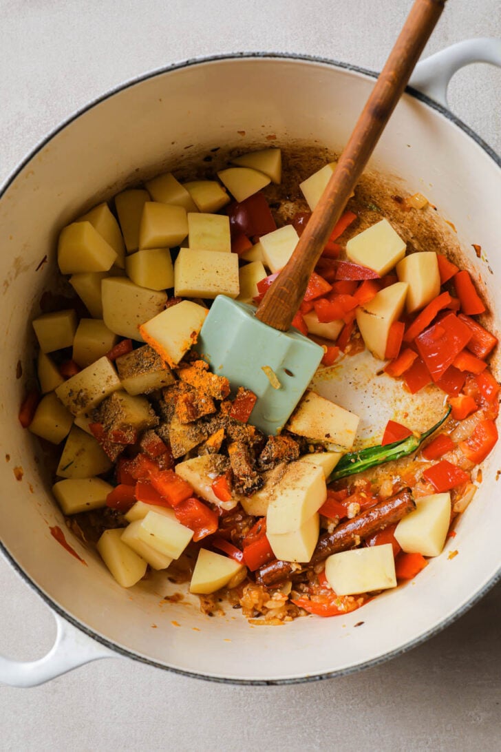 Cubed potato and red bell pepper added to Dutch oven with onion-tomato mixture.