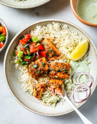Top view of a partially eaten plate of Salmon Tikka with rice, vegetables, onion and lemon.