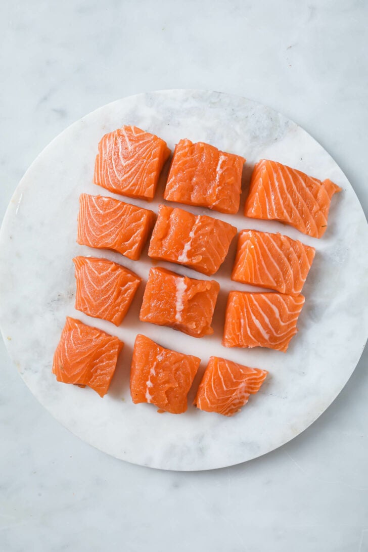 Raw salmon cut into cubes on a marble slab.