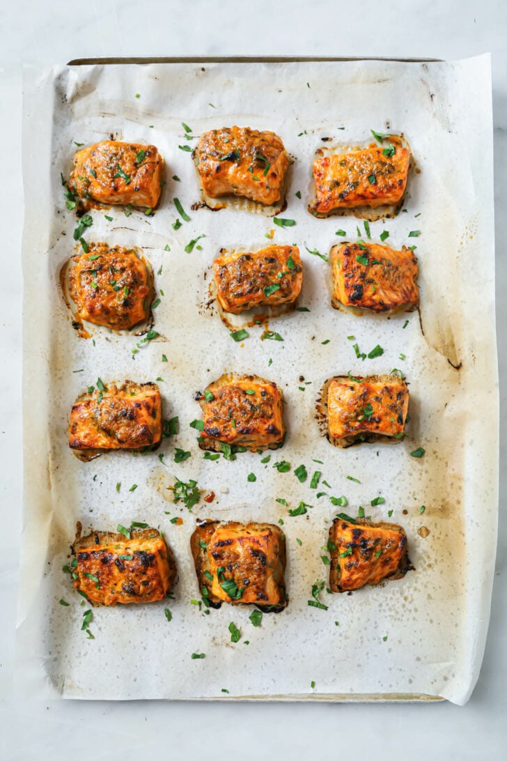 A parchment covered sheet pan with baked Salmon Tikka sprinkled with parsley.