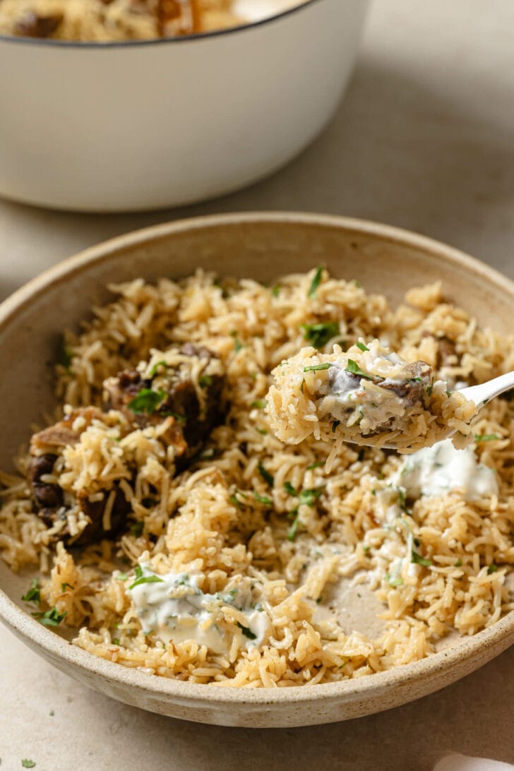 Holding a spoonful of Mutton Pulao with some raita on top.