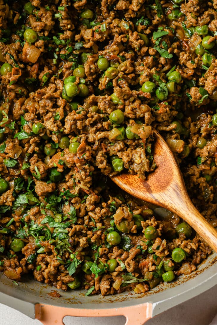 Close up of Keema Matar in a skillet with a wooden spoon.