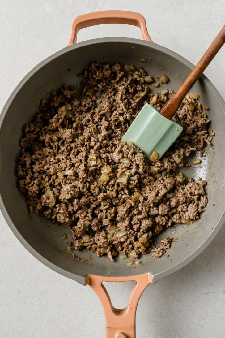 Sauteed ground beef in a skillet with a rubber spatula for Keema Matar.