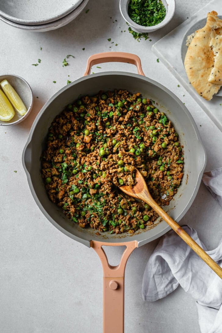 Keema Matar in a skillet with a wooden spoon.
