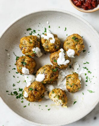 A bowl of Baked Chicken Kofta garnished with raita and chopped cilantro with chutney on the side.