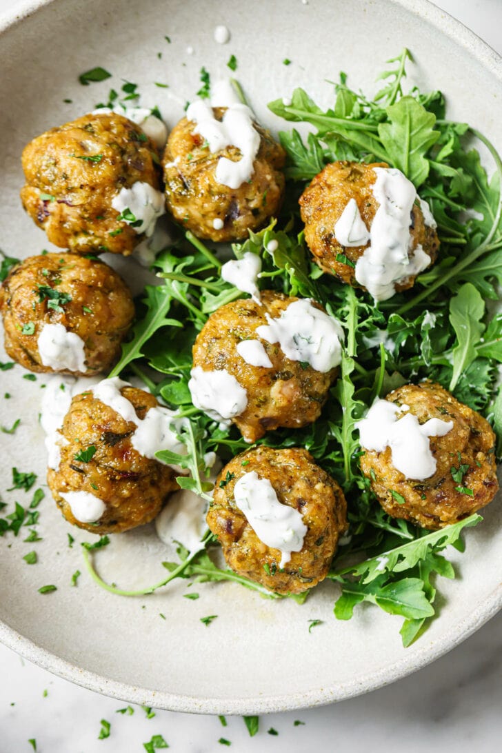 Top view of a bowl of Baked Chicken Kofta garnished with raita, chopped cilantro and arugula.