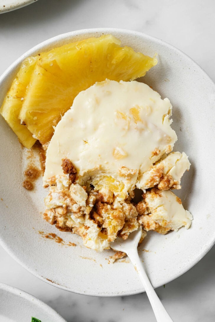 Partially eaten serving of Crushed Pineapple Dessert in a white plate with sliced pineapples on the side.