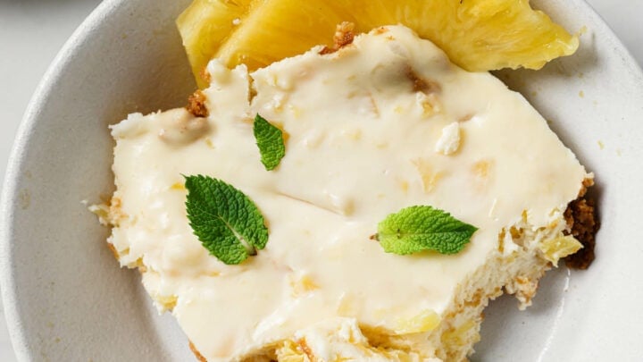 A serving of Crushed Pineapple Dessert in a white plate with sliced pineapples on the side.