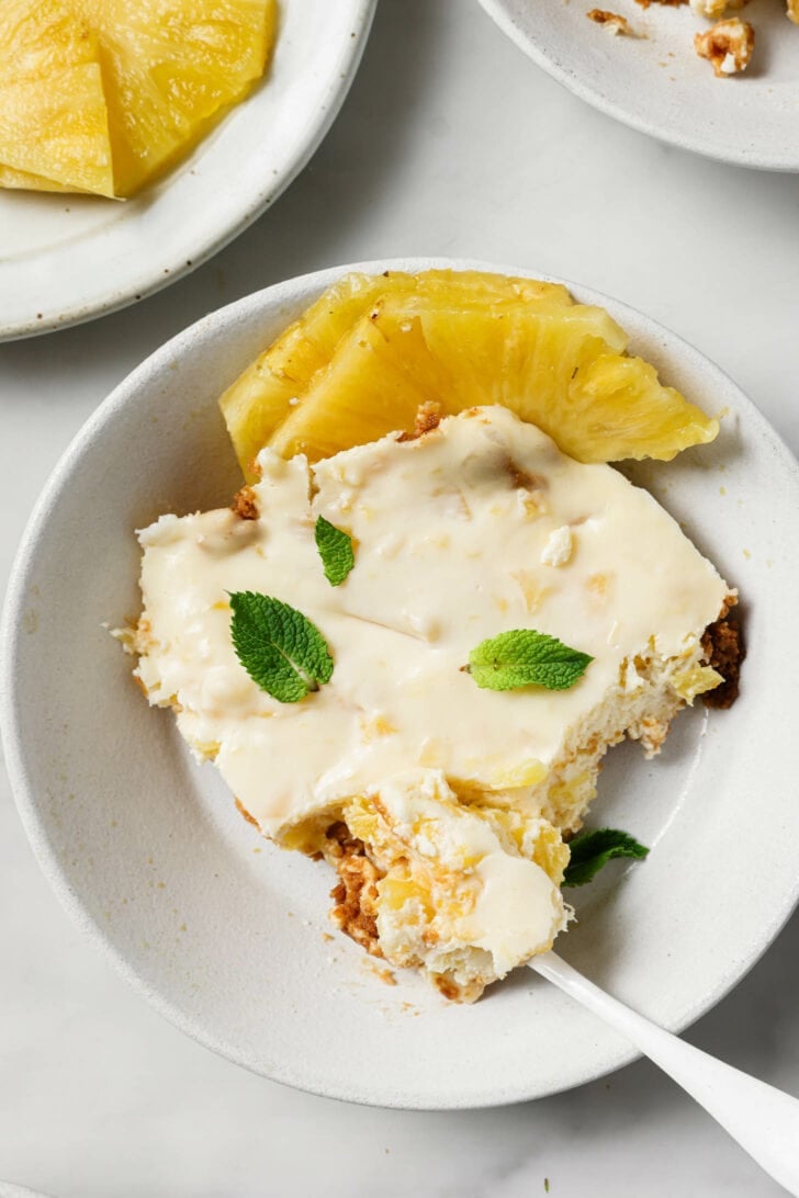 A serving of Crushed Pineapple Dessert in a white plate with sliced pineapples on the side.