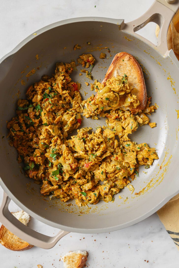 Partially eaten Egg Bhurji in a skillet with half a slice of toast.