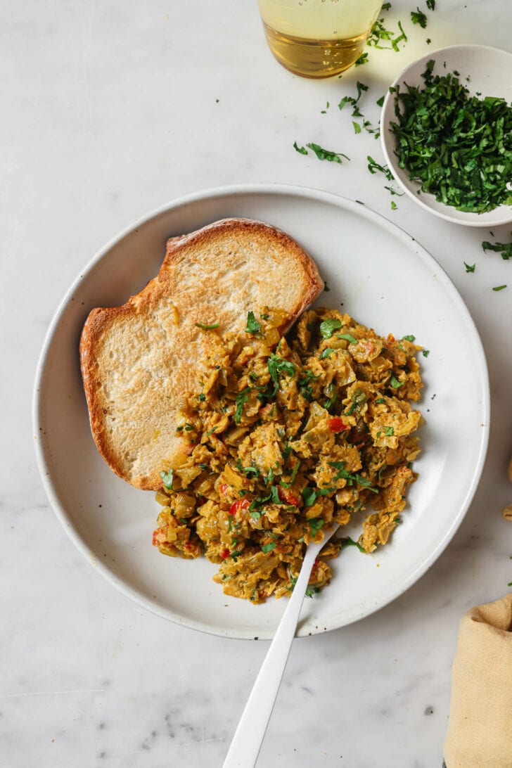 A plate of Egg Bhurji garnished with cilantro alongside a piece of toast.