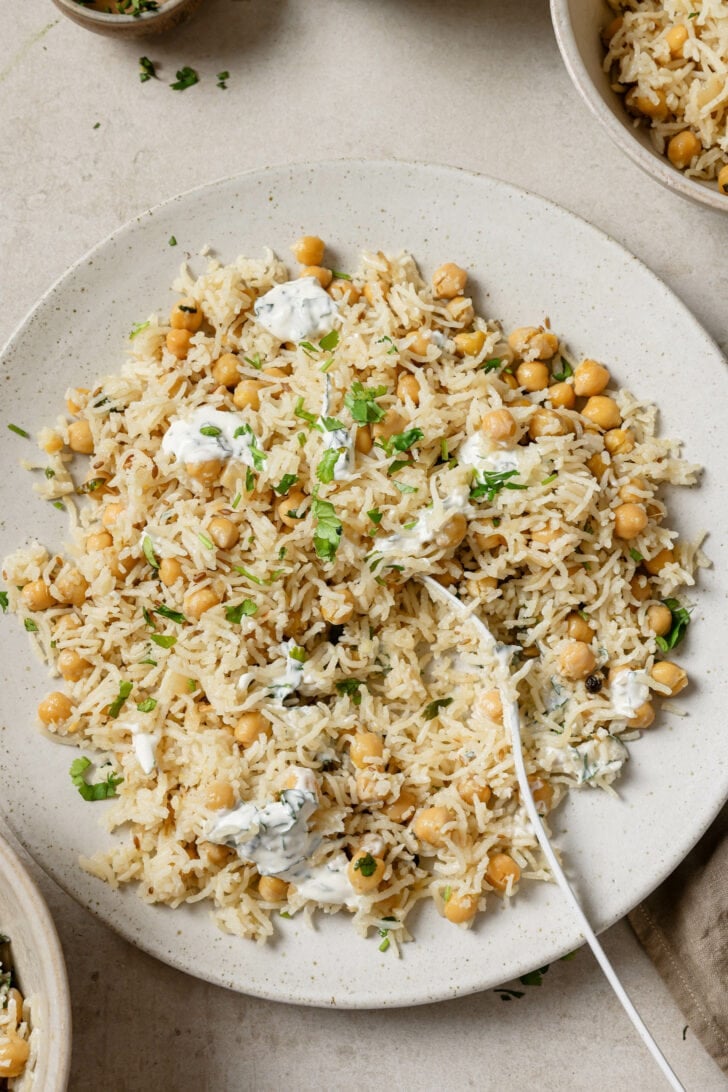 Partially eaten plate of Chana Pulao with raita and garnished with cilantro.